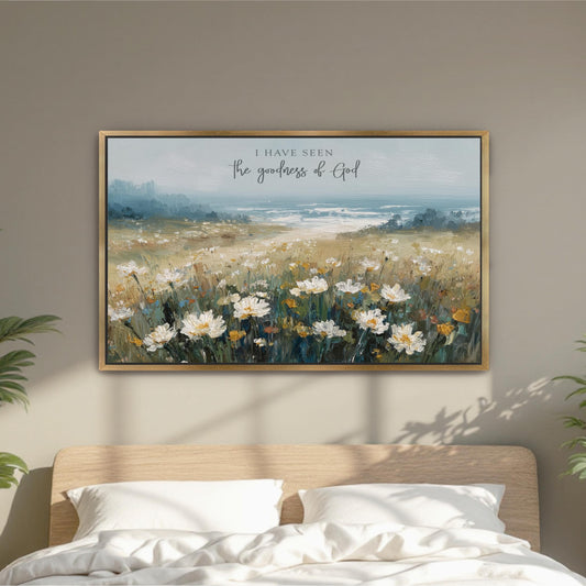 a framed painting of a field of white flowers hanging on a wall above a bed with white pillows.