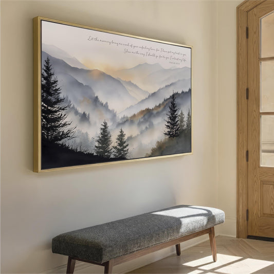 a large framed landscape painting hanging on a wall, depicting a serene mountain scene with pine trees and a hazy, golden sky. In the foreground, there is a gray bench positioned against the wall, providing a seating area for viewers to appreciate the artwork.