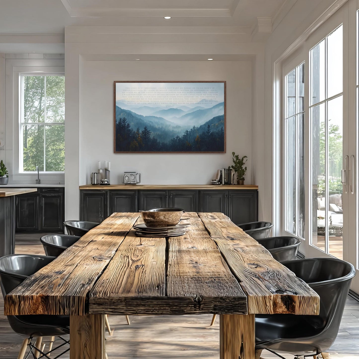 a modern dining room with a large wooden table surrounded by black chairs. The table is set with a bowl and plates, and a framed landscape painting hangs on the wall above it. The room has large windows that provide ample natural light, and the overall design has a contemporary and minimalist aesthetic.