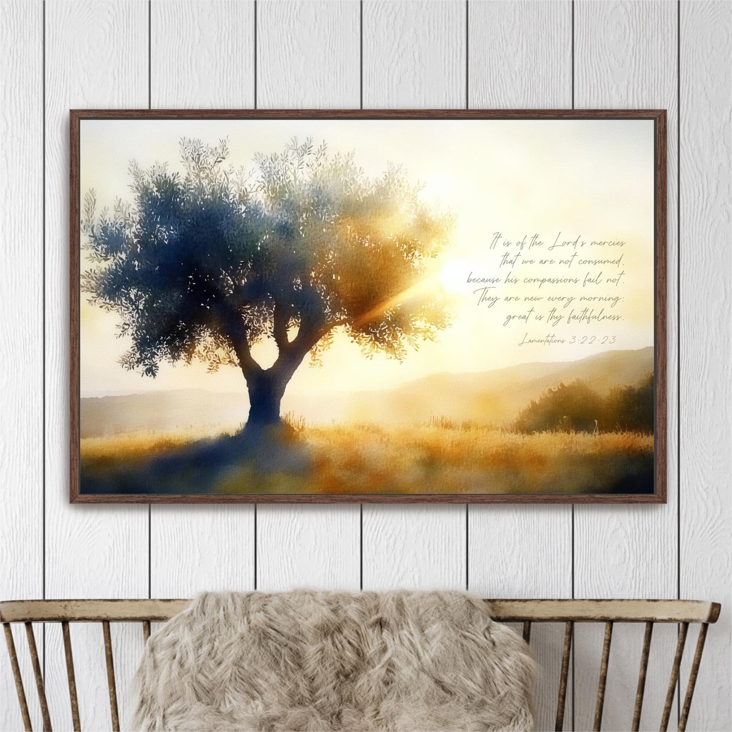 The image is a framed painting depicting a serene landscape with a large tree silhouetted against a warm, golden sunset. The painting is hung on a white wall above a wooden bench, creating a peaceful and tranquil atmosphere.