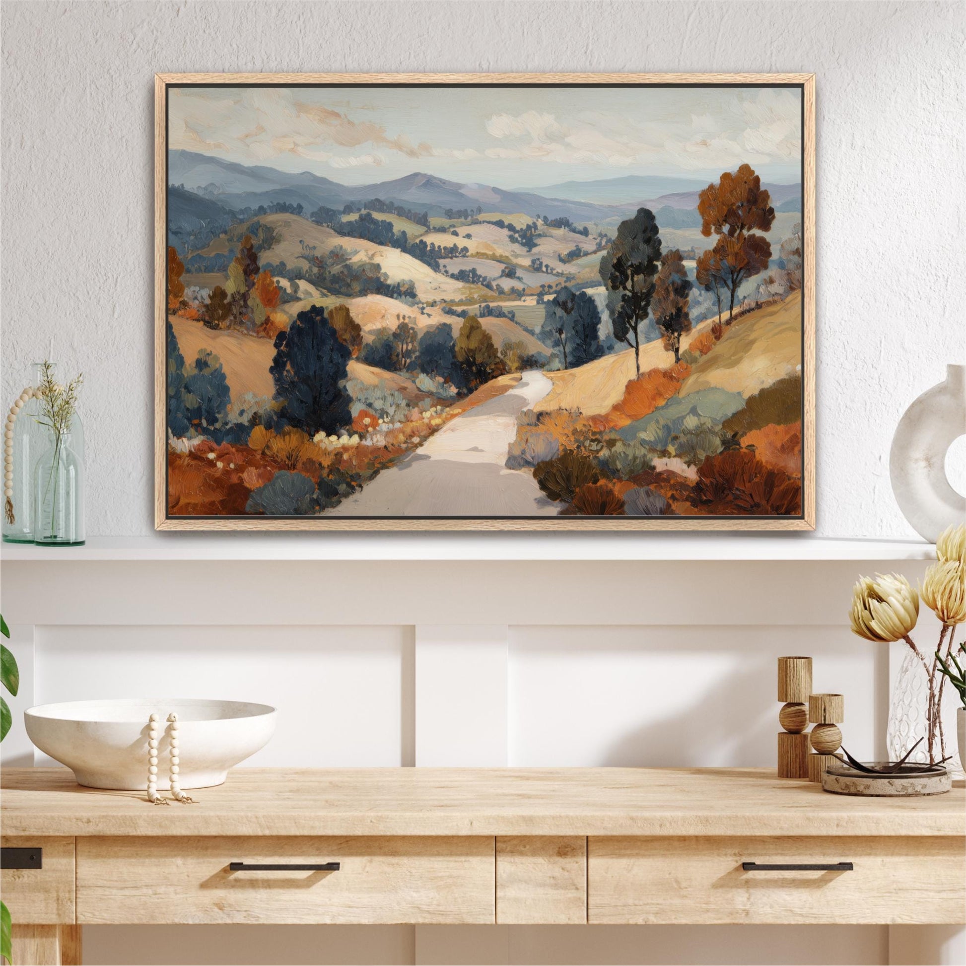 a large landscape painting hanging on a wall above a wooden table with various decorative items on it.