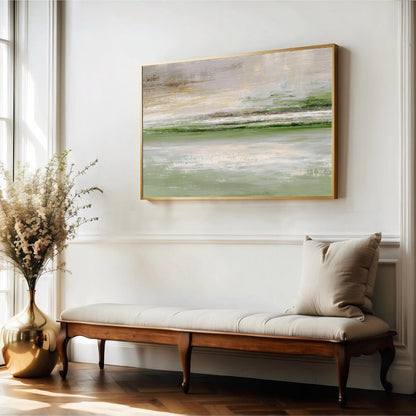 a large, framed painting of a landscape hanging on a white wall above a wooden bench with a beige cushion. The painting depicts a serene, natural scene with a body of water and a sky with a pale green hue. The room has a clean, minimalist aesthetic with white walls and a wooden floor.
