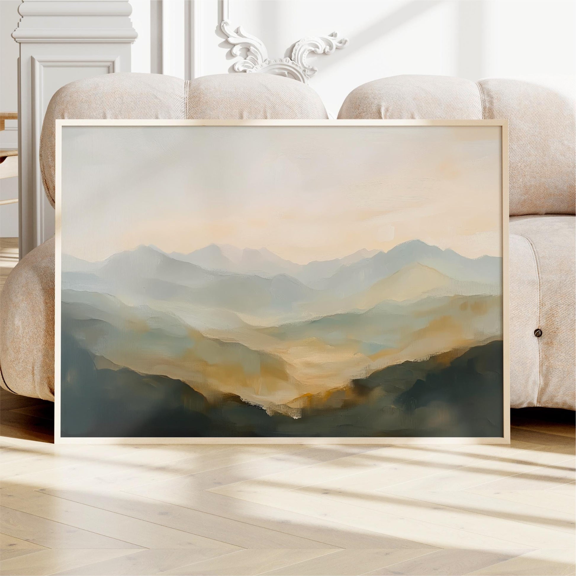 a large framed painting of a mountainous landscape, displayed on a wooden floor in front of a white couch.