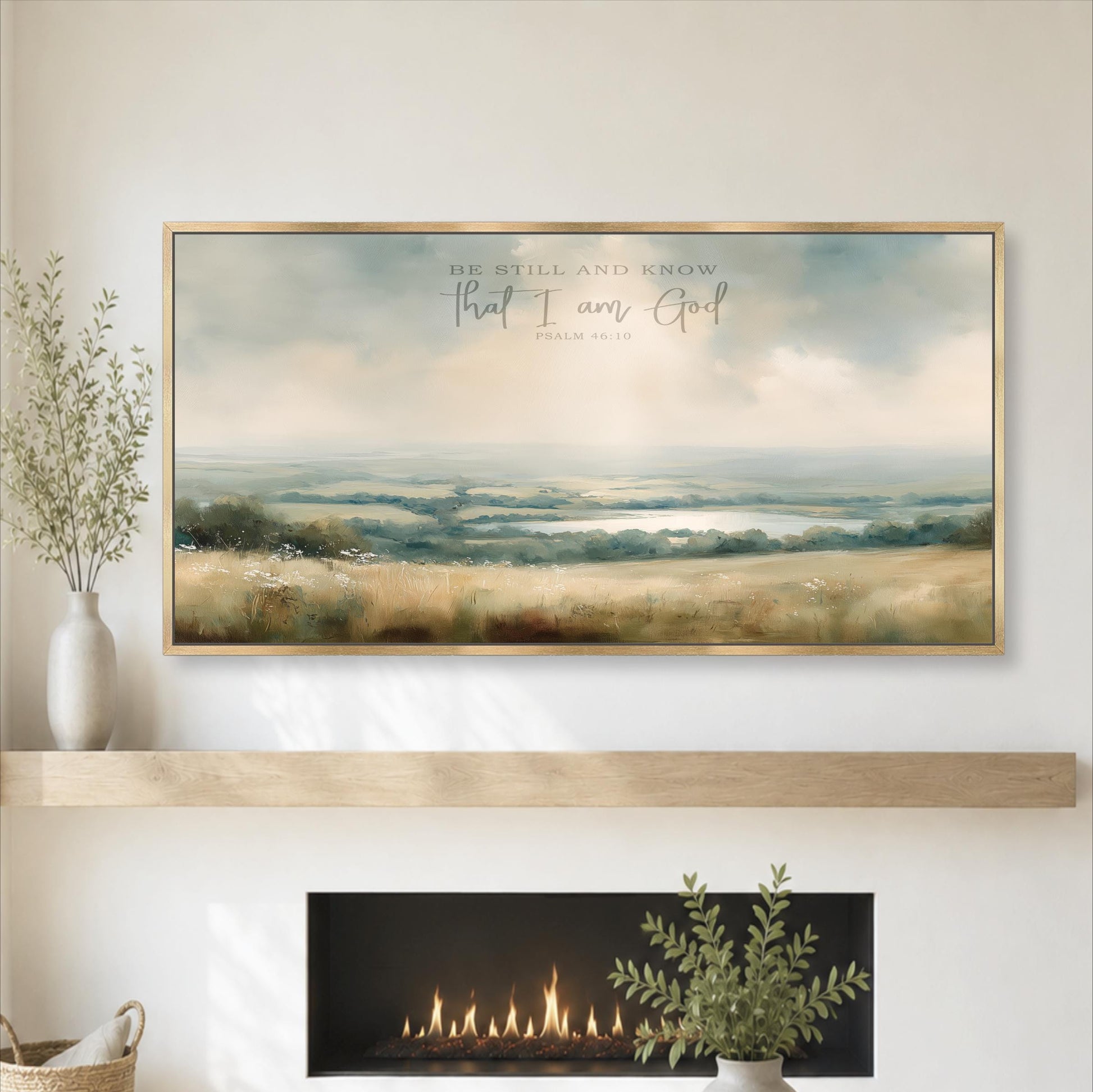 a large framed painting of a serene landscape with a field and a body of water, hanging above a fireplace with a vase of greenery on the mantel.