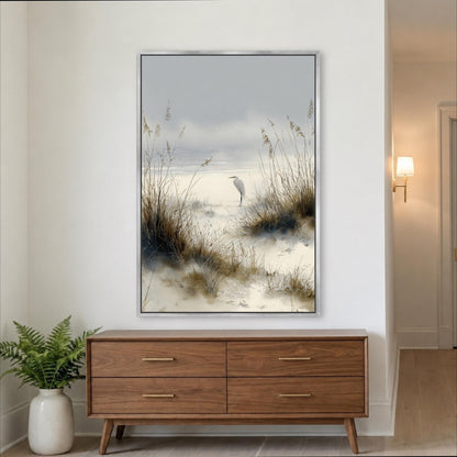 a large framed painting of a bird standing on a beach, with tall grasses in the foreground and a calm body of water in the background. The painting is hung on a white wall above a wooden dresser with four drawers.
