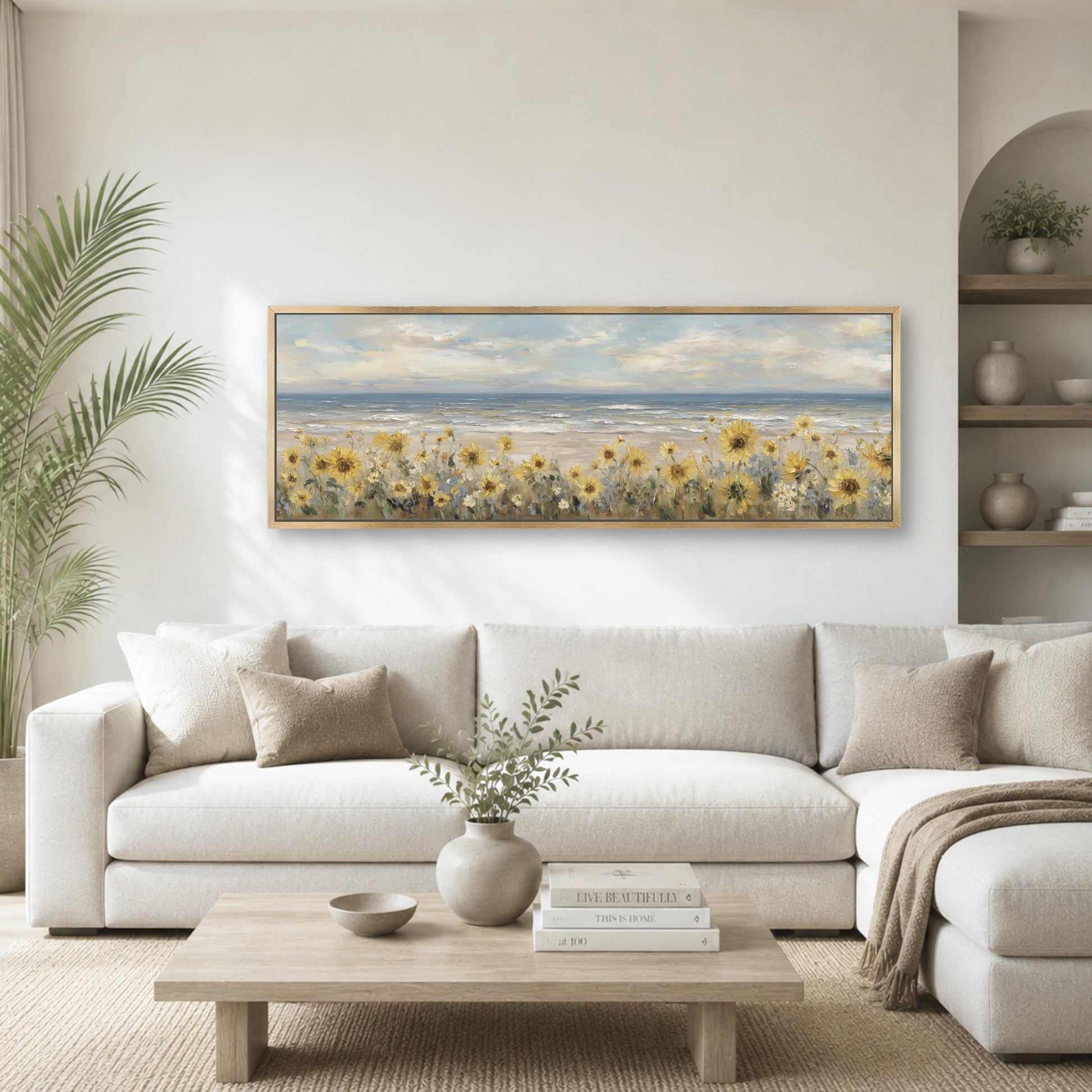 a serene living room with a large painting of a field of yellow flowers hanging on the wall above a white sofa. The sofa is positioned in front of a wooden coffee table, which has a vase of greenery and a stack of books on it. The room also features a potted plant and a bookshelf, creating a cozy and inviting atmosphere.