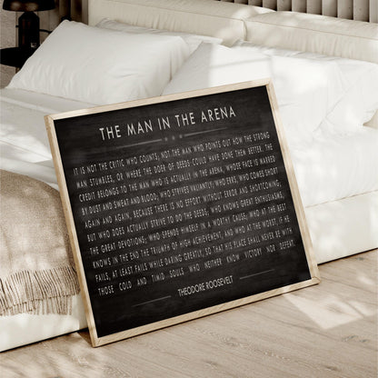 a framed quote by Theodore Roosevelt, which is displayed on a bed with a white comforter.