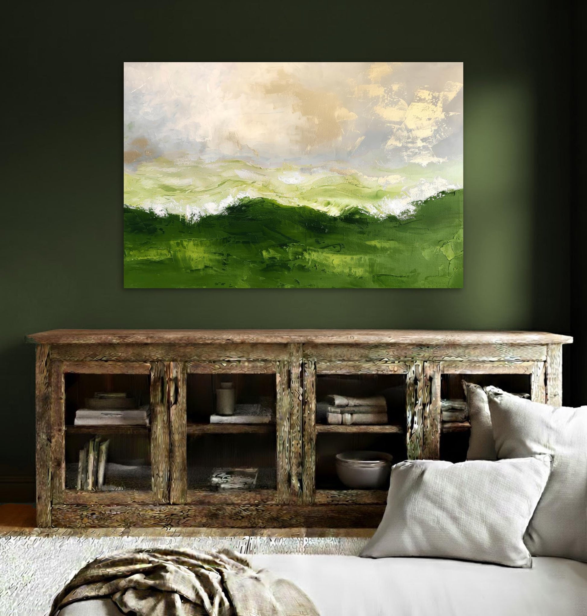 a large, vibrant painting of a green landscape hanging on a wall above a wooden cabinet with glass doors. The cabinet has several books and decorative items displayed on its shelves. The room has a cozy, inviting atmosphere with a couch and a rug in the foreground.