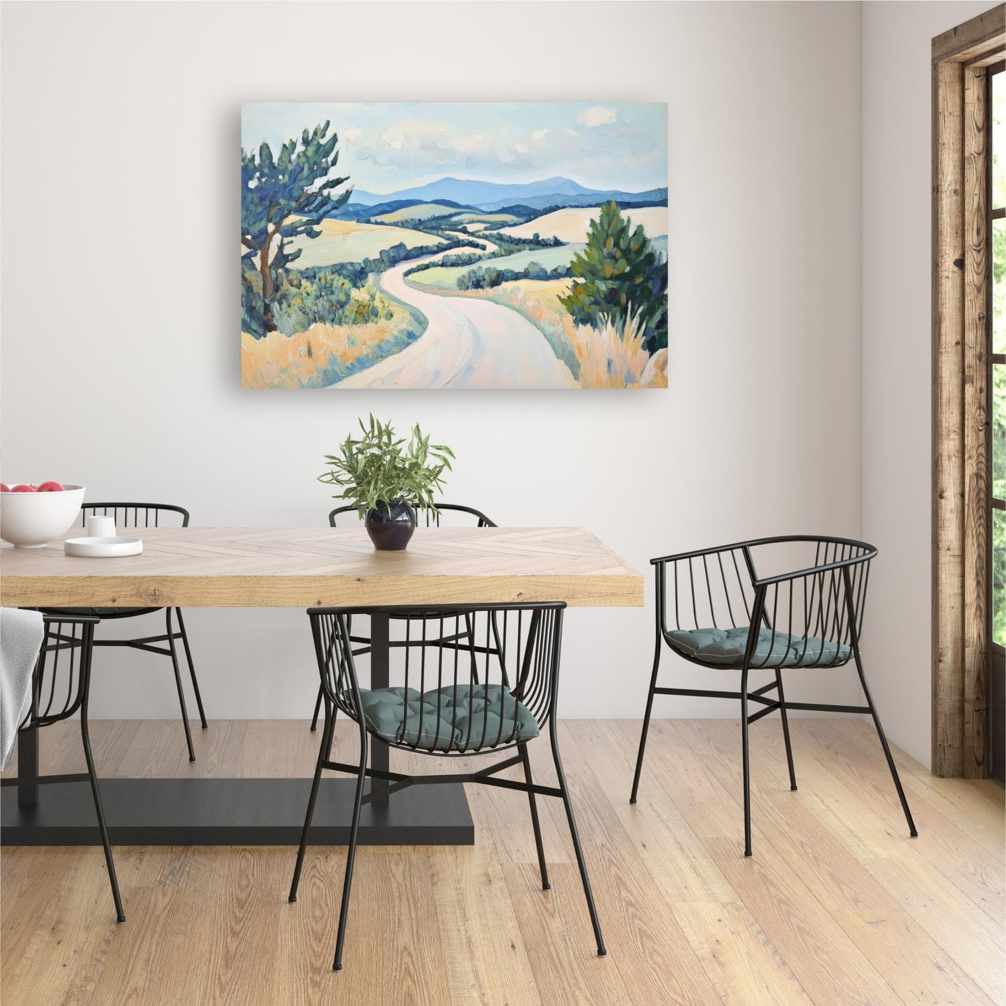 a dining room with a wooden table and chairs, a painting of a countryside landscape hanging on the wall, and a potted plant on the table.