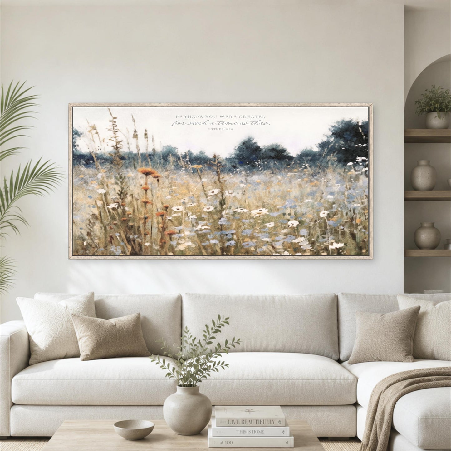 a large, framed painting of a field with tall grass and wildflowers hanging on a wall above a white couch in a living room.