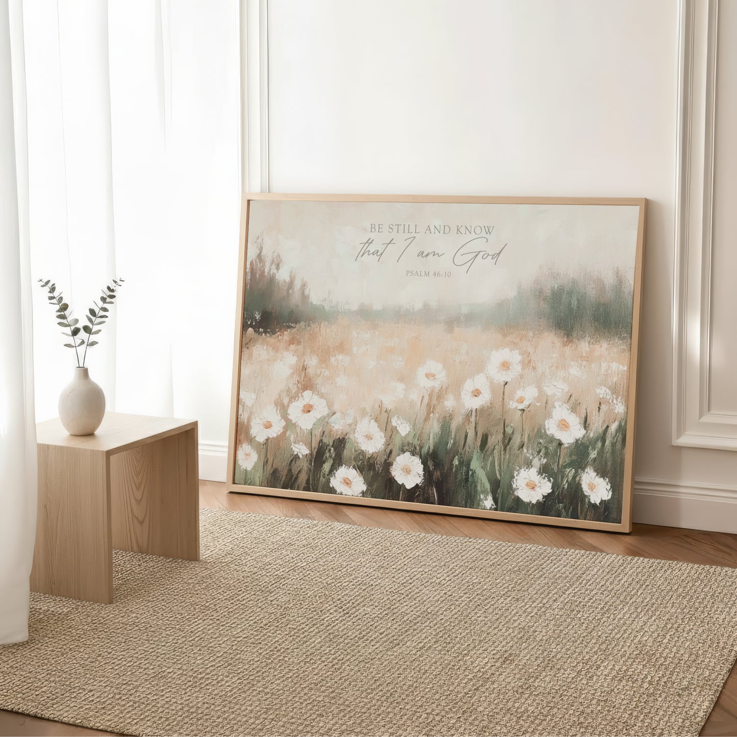 a large framed print of a field of white flowers, with a vase of greenery placed next to it on a wooden table.