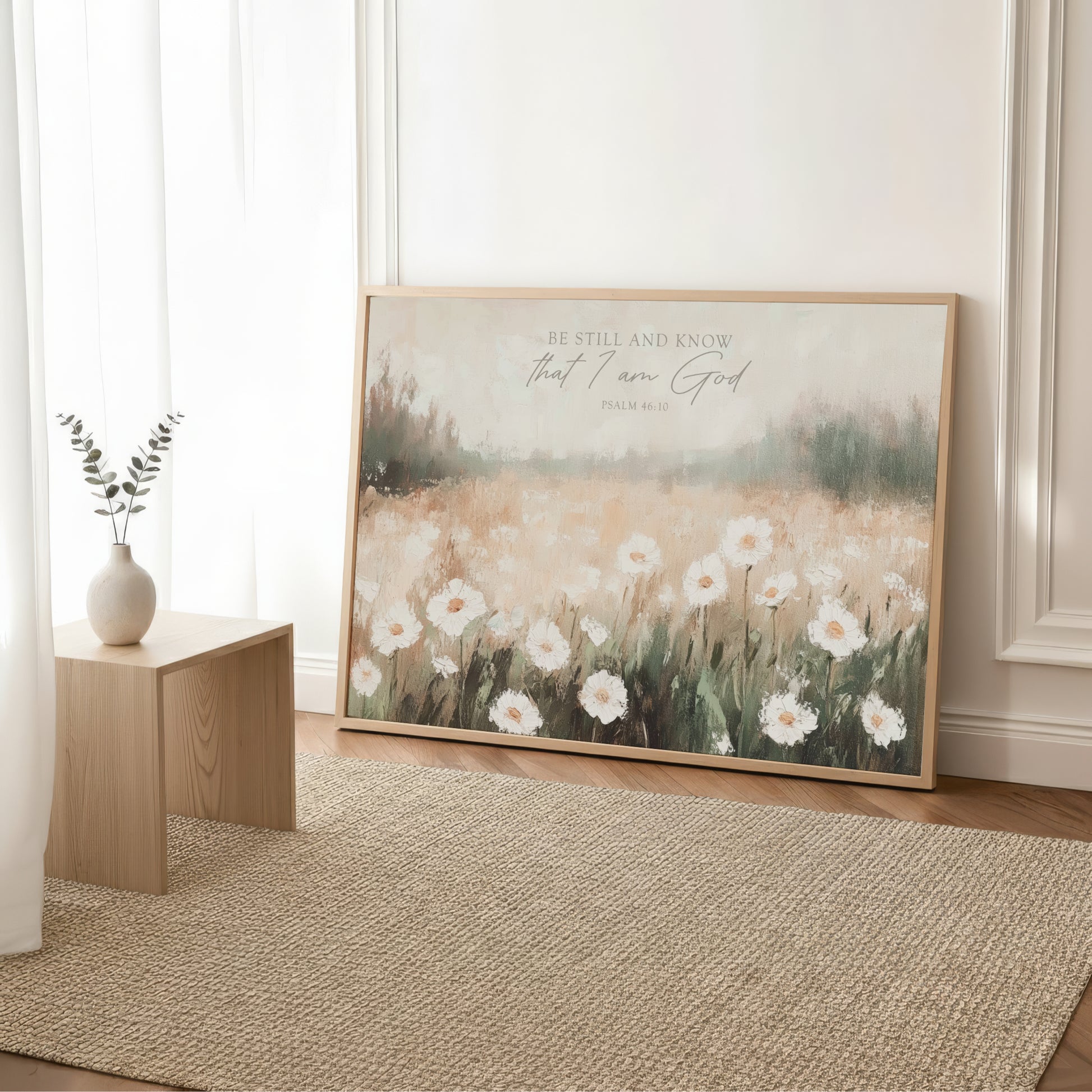 a large framed print of a field of white flowers, with a vase of greenery placed next to it on a wooden table.