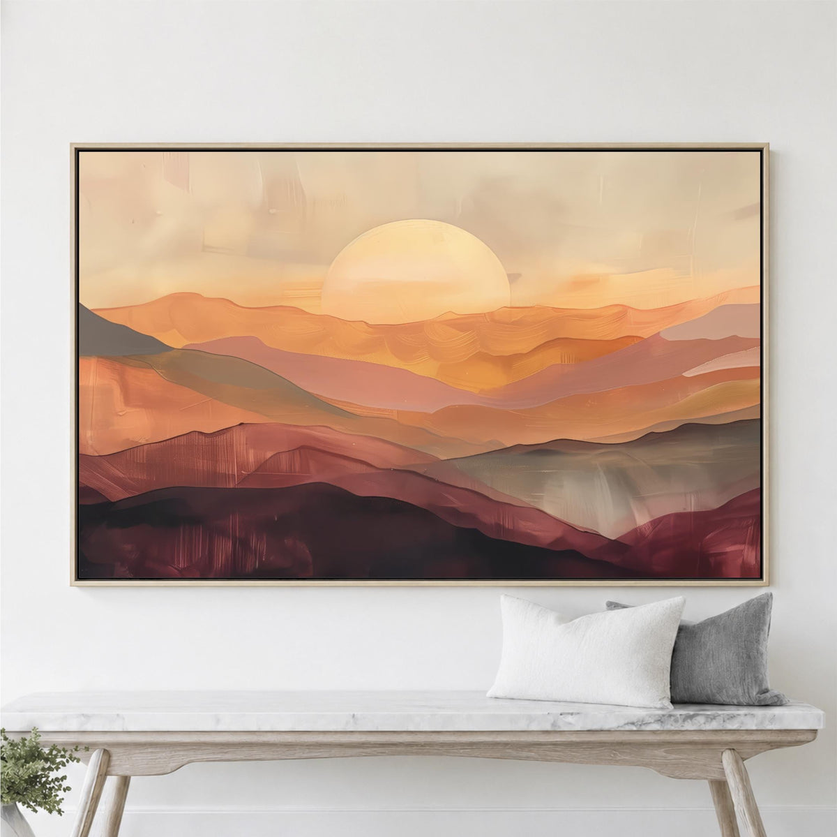 a large, framed painting of a sunset over mountains, hanging on a wall above a wooden bench with two pillows.