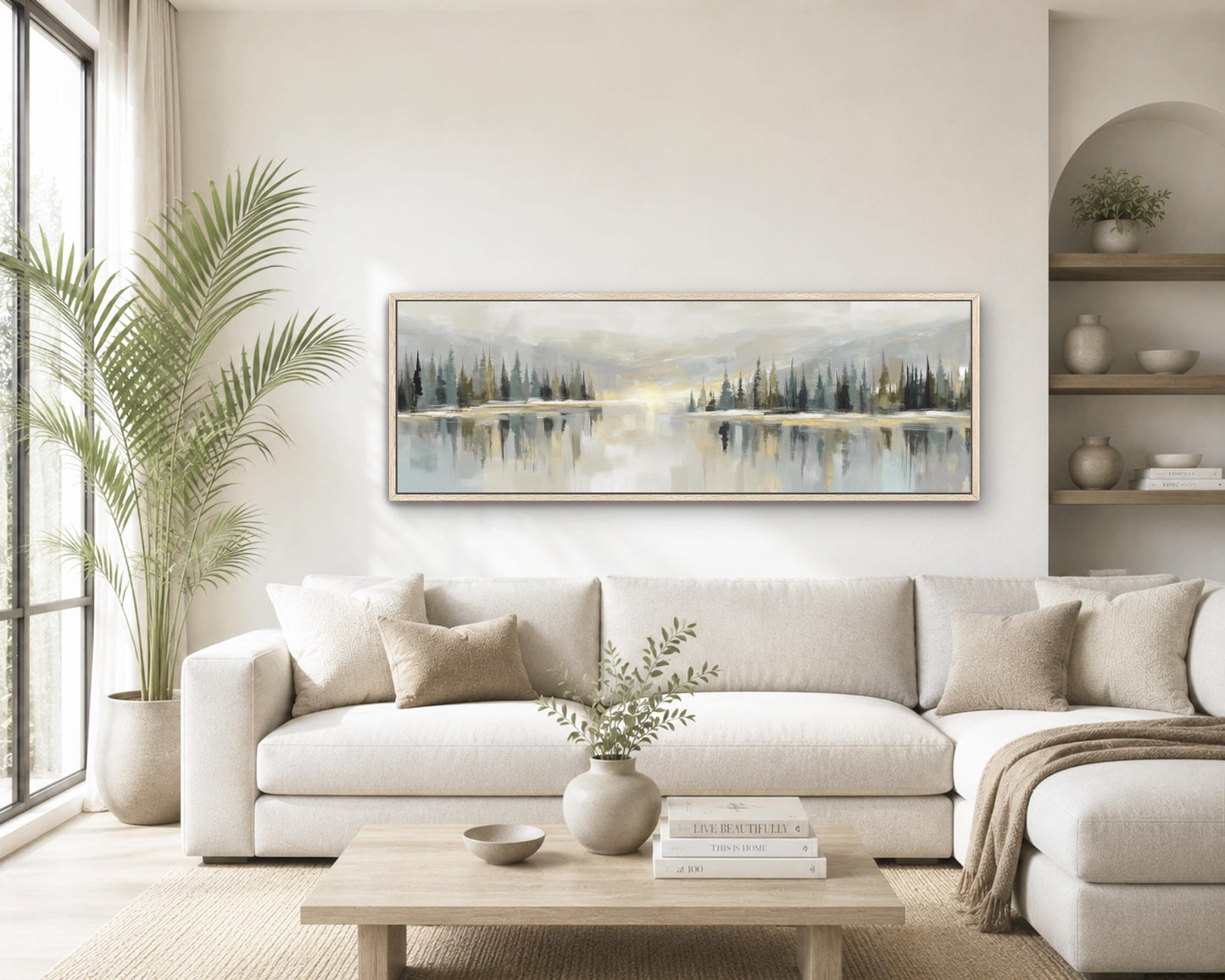a serene living room with a large painting of a landscape featuring a lake and trees hanging on the wall above a white sofa. The room is decorated with a potted plant, a vase with greenery, and a stack of books on a coffee table.