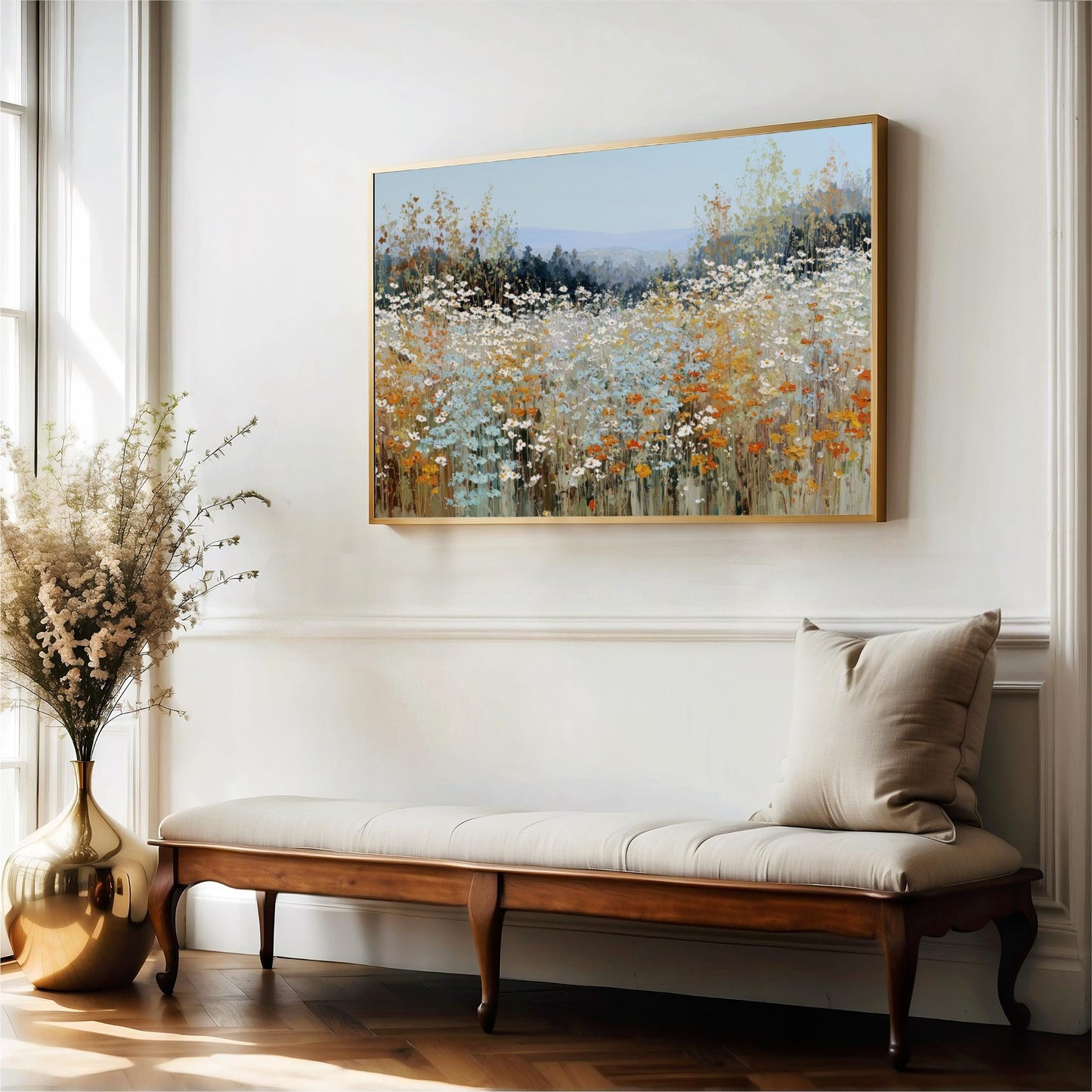 a large painting of a field of flowers hanging on a white wall, with a wooden bench and a vase of flowers placed next to it.