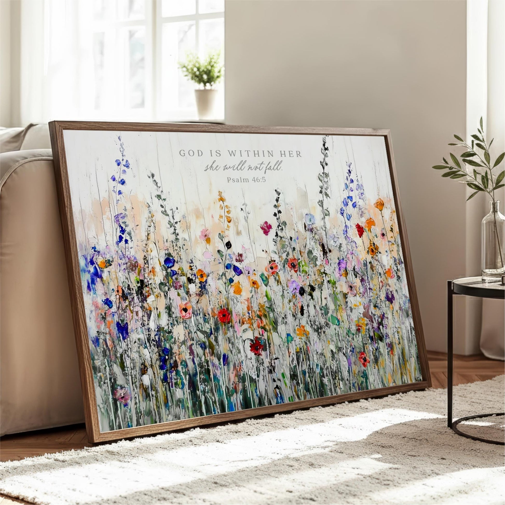 A framed painting of a colorful field of flowers is displayed on a wooden floor in a living room.
