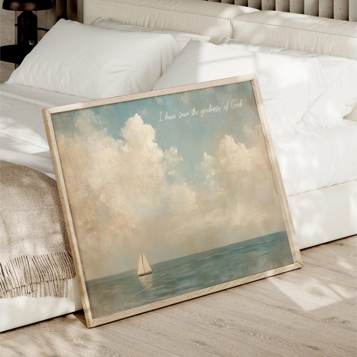 A framed painting of a sailboat on the ocean is displayed on a bed, with a white pillow and blanket nearby.