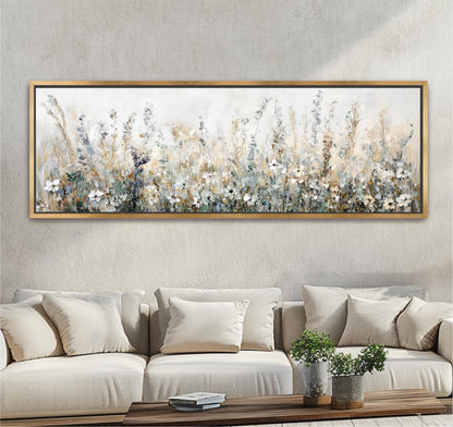 a large, framed painting of a field of flowers hanging on a wall above a beige sofa with white pillows.