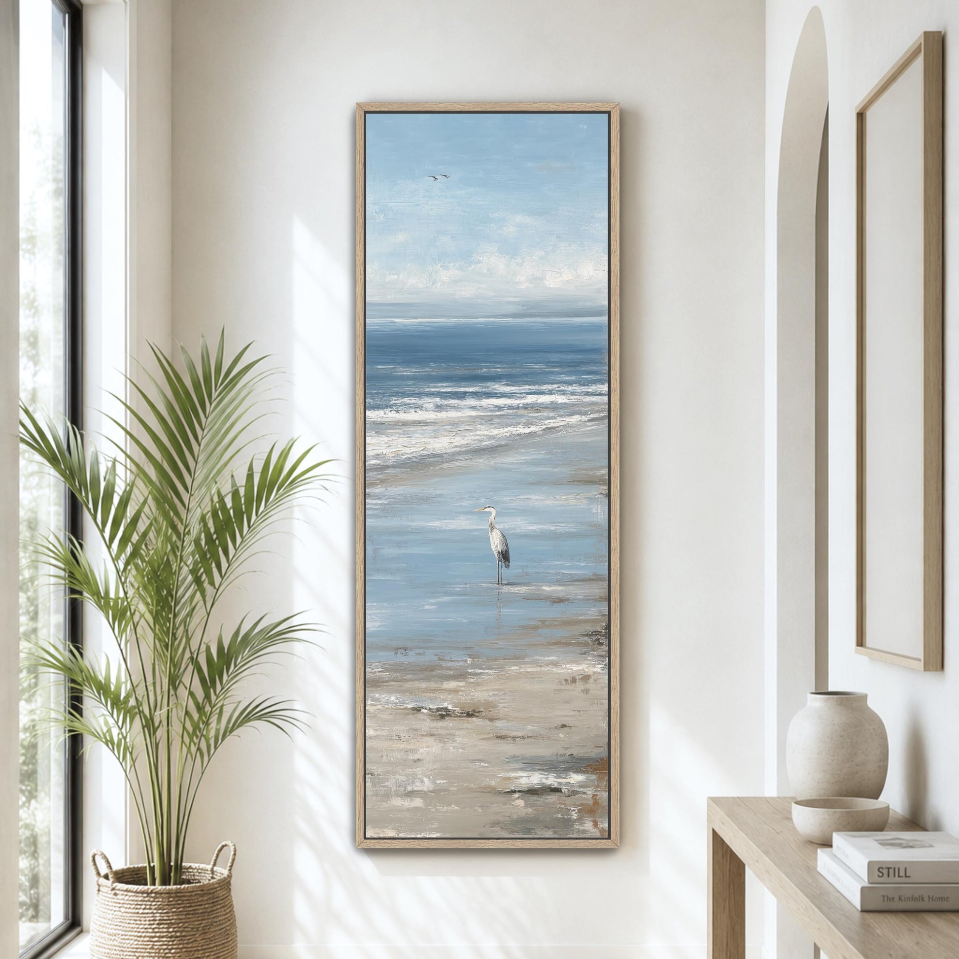 a large painting of a seagull standing on a beach, with the ocean in the background. The painting is hung on a wall, and there is a potted plant and a vase on a table nearby.