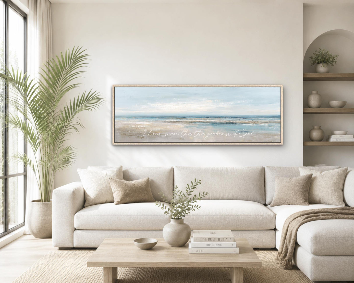 a serene living room with a large white sofa, a wooden coffee table, and a framed painting of a beach scene hanging on the wall.