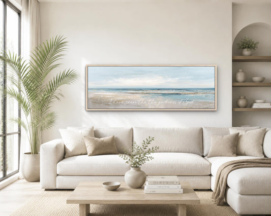 a serene living room with a large white sofa, a wooden coffee table, and a framed painting of a beach scene hanging on the wall.