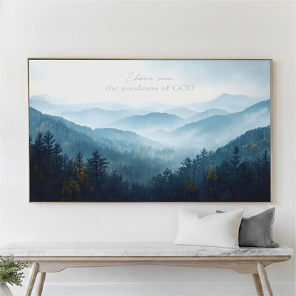a large framed picture of a mountain landscape with trees and fog, hanging on a wall above a wooden bench with pillows.