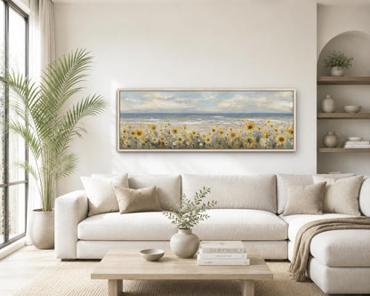 a serene living room with a large painting of a field of sunflowers hanging on the wall above a white sofa. The sofa is positioned in front of a wooden coffee table, which has a vase of greenery and a stack of books on it. The room also features a large window, a potted plant, and a bookshelf with various decorative items.