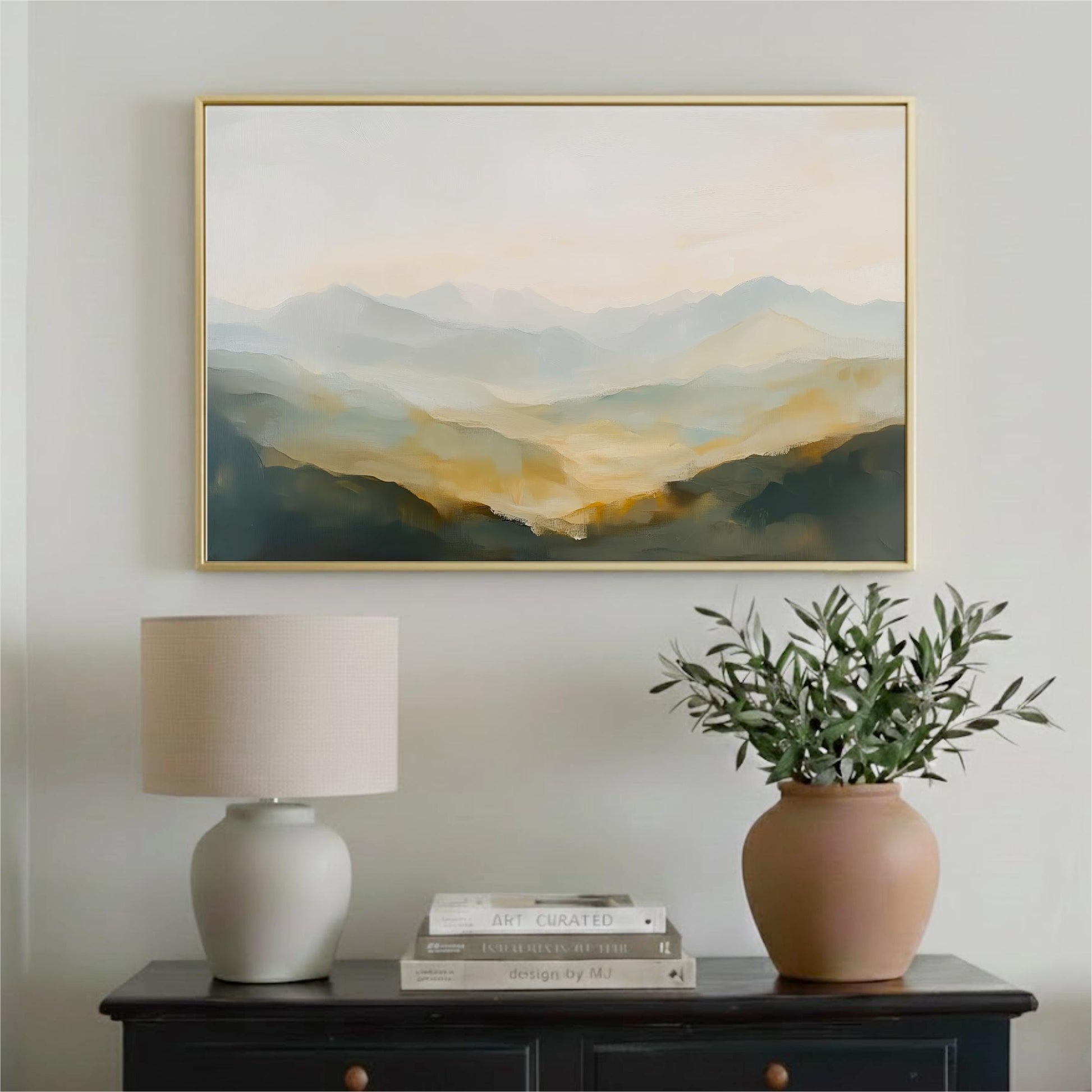 a framed landscape painting hanging on a wall above a black dresser with a lamp and a vase of greenery.