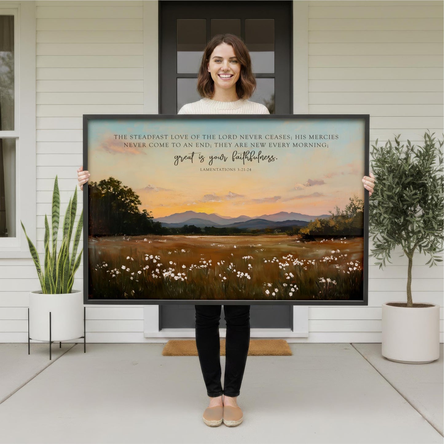 A woman stands in front of a large painting depicting a serene landscape with mountains, flowers, and a sunset.