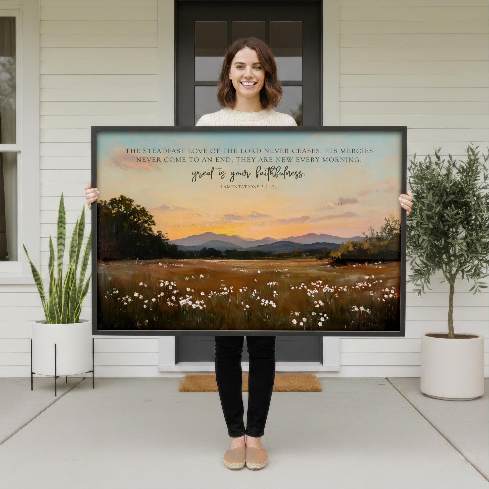 A woman stands in front of a large painting depicting a serene landscape with mountains, flowers, and a sunset.