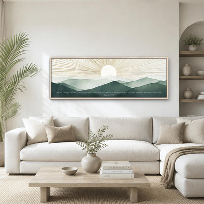 a living room with a large framed landscape painting hanging on the wall above a white sofa. The painting depicts a serene mountain landscape with a sun rising over the horizon. The room is decorated with a wooden coffee table, a potted plant, and a vase with greenery.