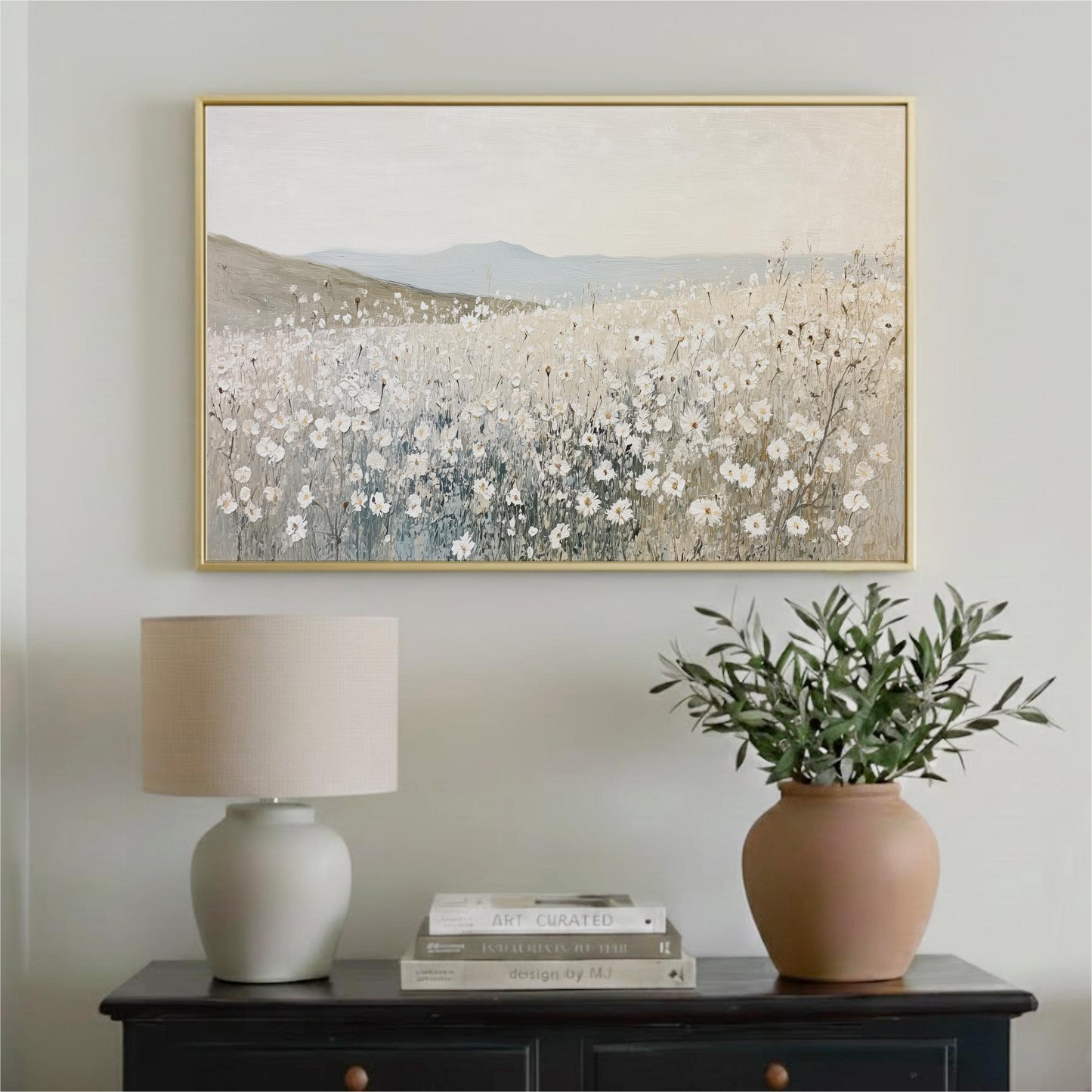 a painting of a field of flowers hanging on a wall above a black dresser with a lamp and a vase of greenery.