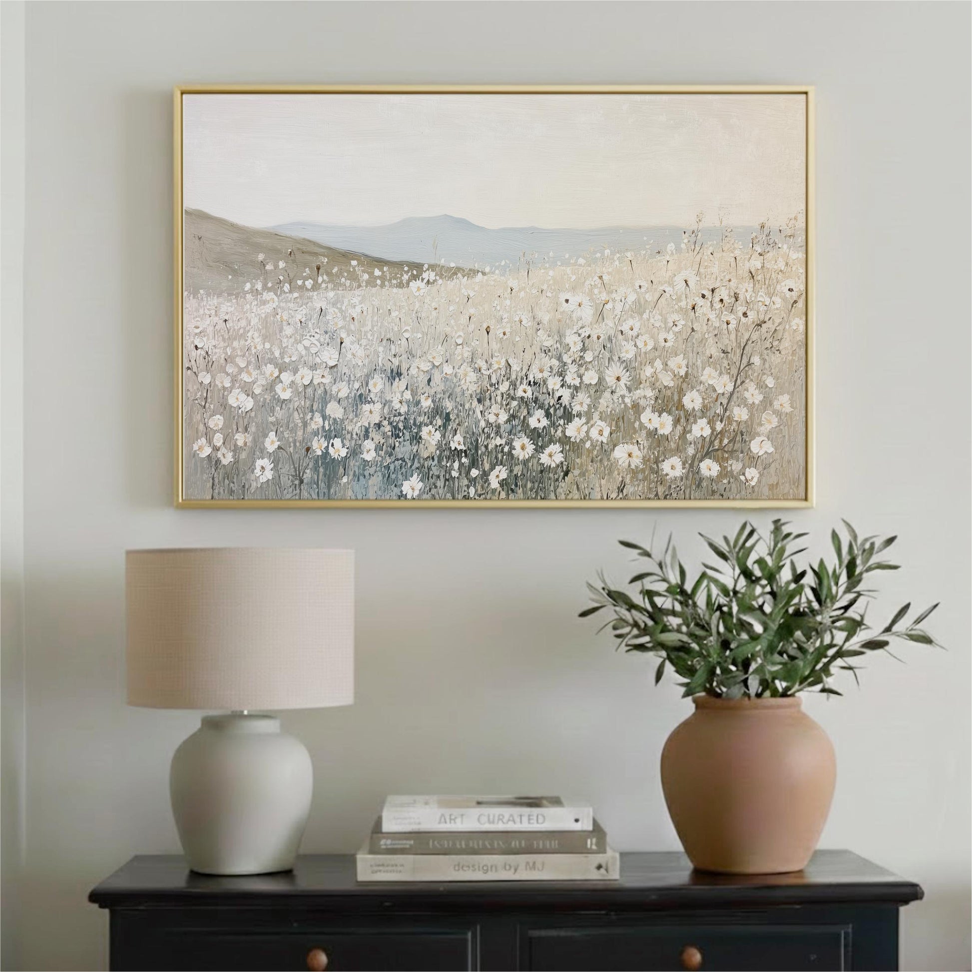 a painting of a field of flowers hanging on a wall above a black dresser with a lamp and a vase of greenery.