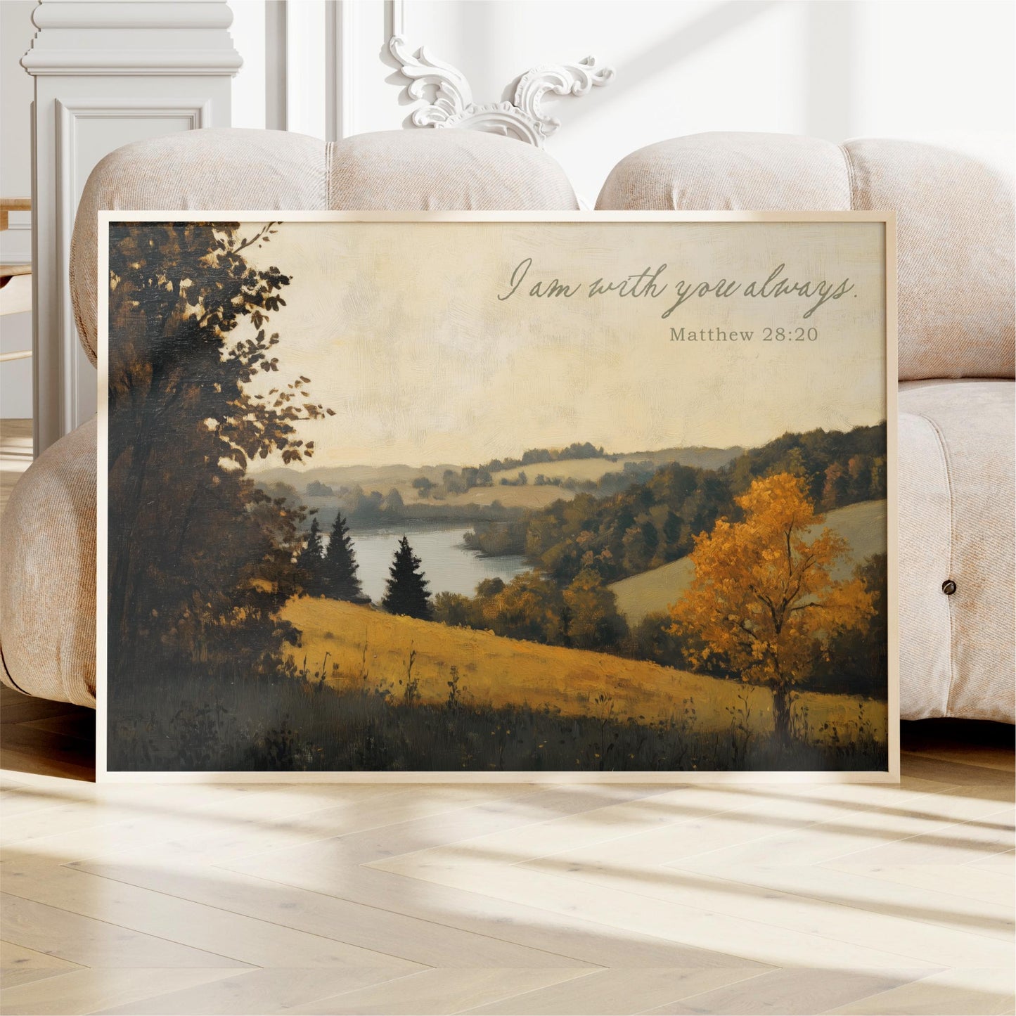 a framed painting of a serene landscape with trees, grass, and a body of water. The painting is displayed on a white couch in a room with a white wall and a decorative molding.