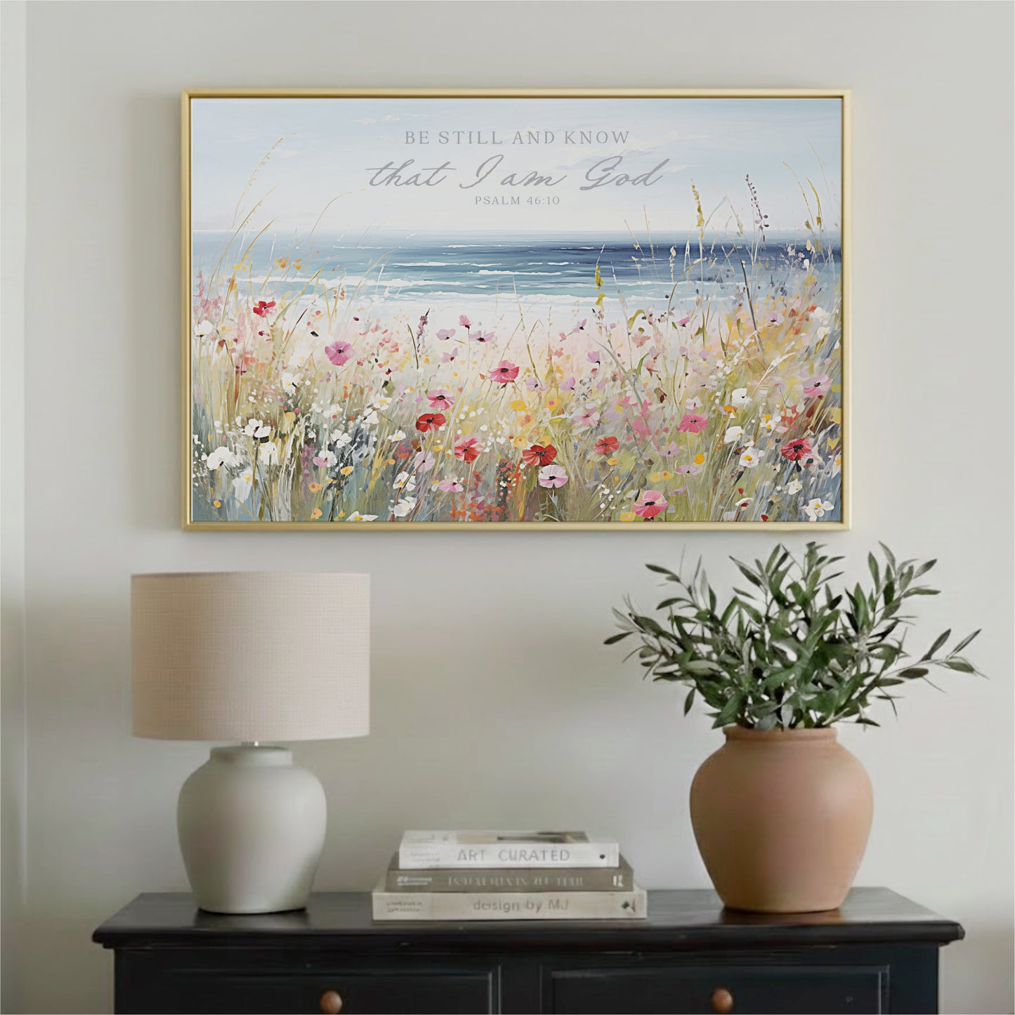 a framed painting of a field of flowers hanging on a wall above a wooden table with a lamp and a potted plant.