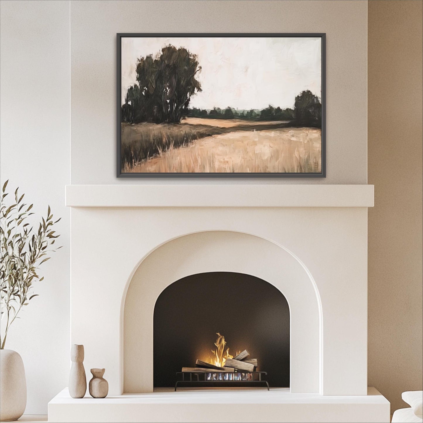 a cozy living room with a white fireplace and a framed landscape painting above it. The painting depicts a serene countryside scene with trees and a field. The fireplace has a black screen and a fire burning inside, creating a warm and inviting atmosphere in the room.