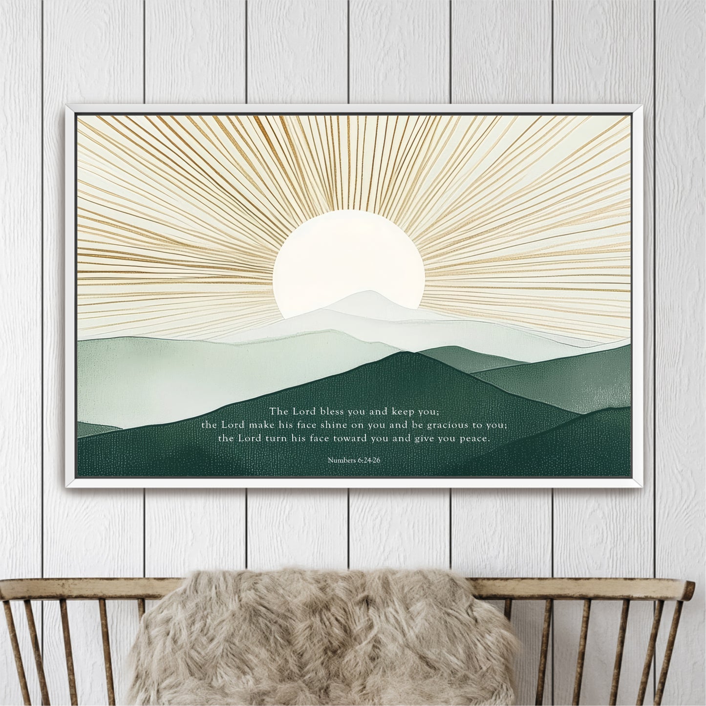 The image is a framed artwork depicting a serene landscape with a sun rising over a mountain range. The sun is the central focus, radiating light across the scene. The mountains in the background are a mix of green and gray, creating a sense of depth and distance. The text "The Lord Bless you and keep you, the Lord make his face shine on you and begraceful to you; he gives you peace" is displayed below the sun, providing a spiritual message.