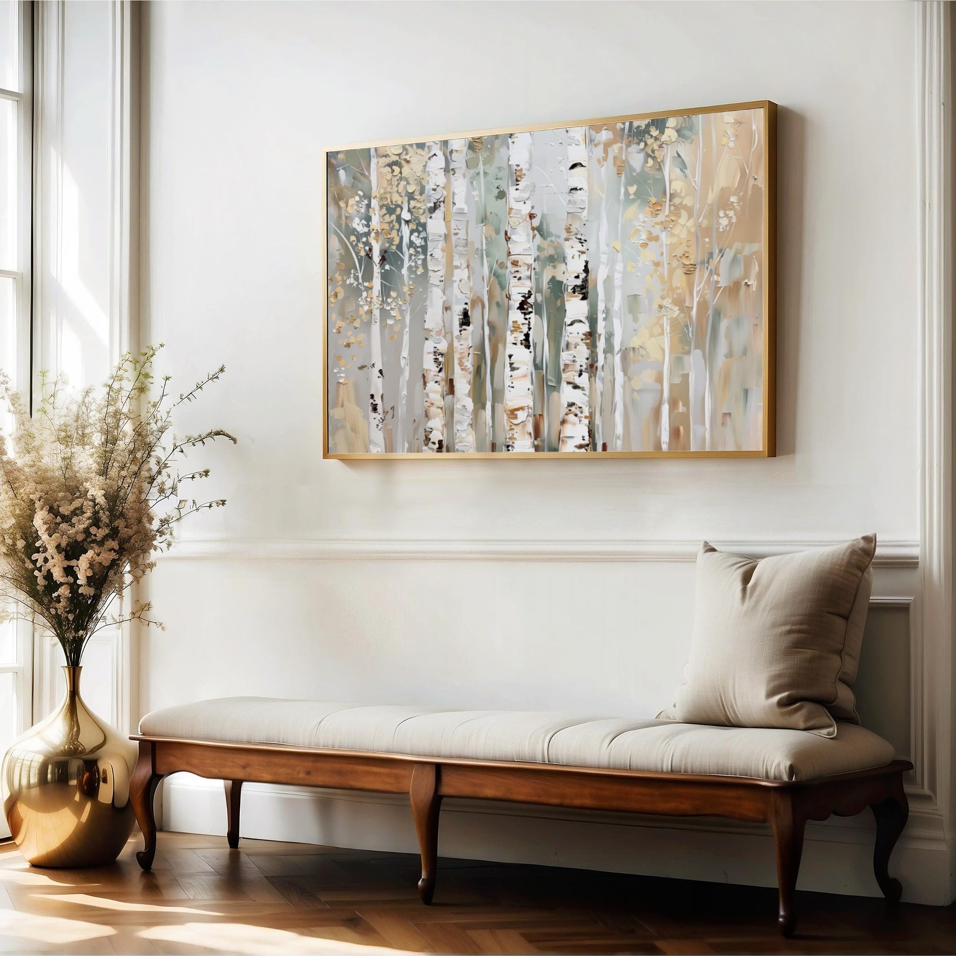 a wooden bench with a beige cushion, positioned in front of a large painting of birch trees on a white wall. The painting is framed in gold and hangs above the bench. The room has a white color scheme, with a large window allowing natural light to illuminate the space.