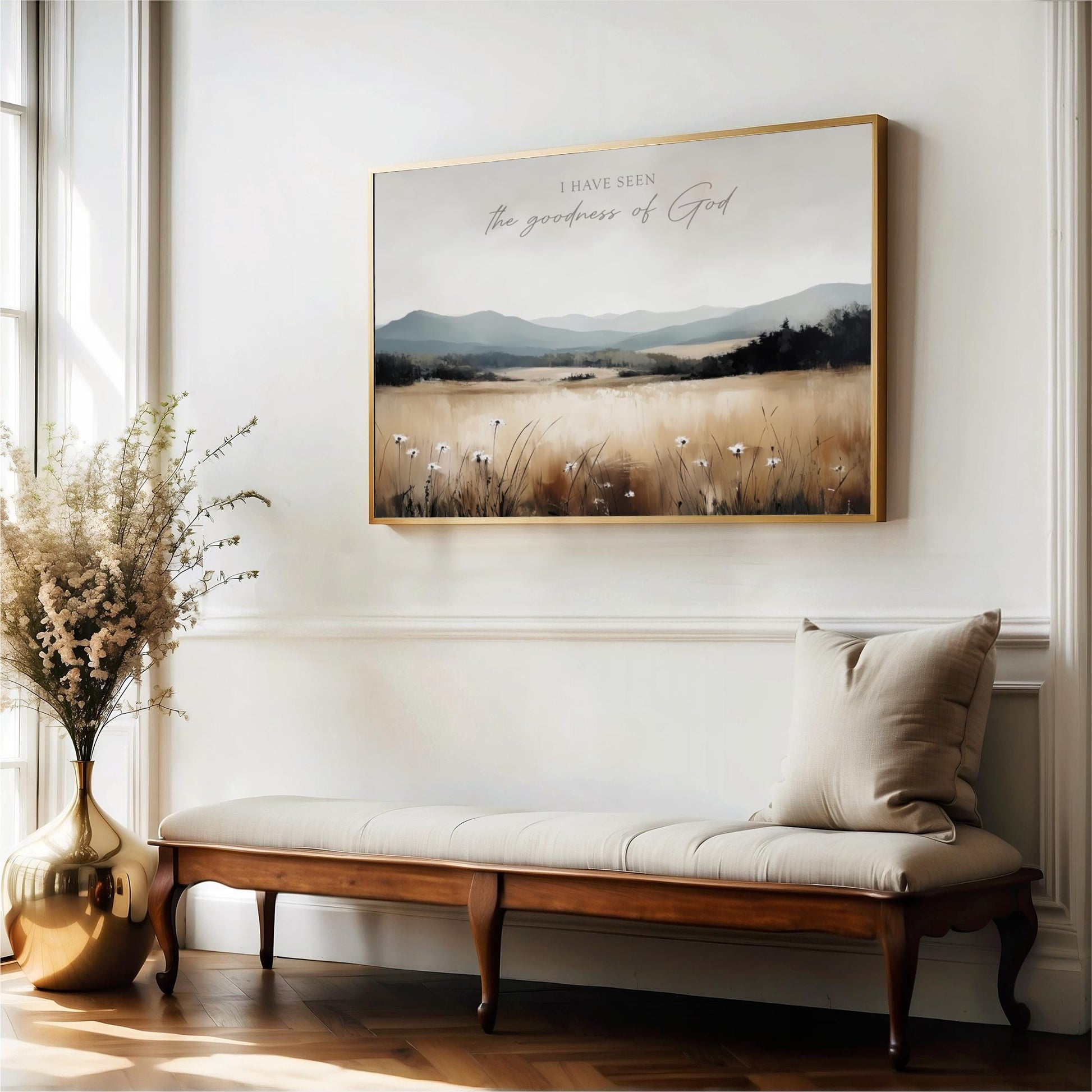 a large framed painting of a field with flowers hanging on a wall above a wooden bench with a beige cushion.