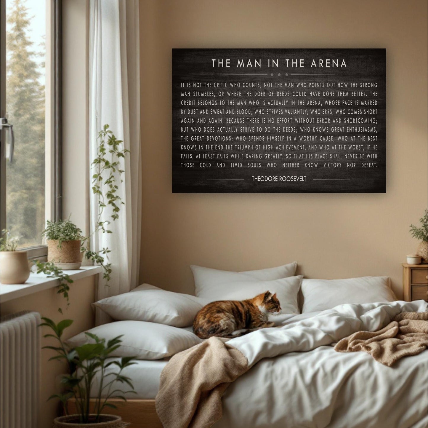 a bedroom with a large black sign hanging on the wall that reads "The Man in the Arena" by Theodore Roosevelt. The sign is surrounded by various objects, including a cat sleeping on the bed, potted plants, and a window.