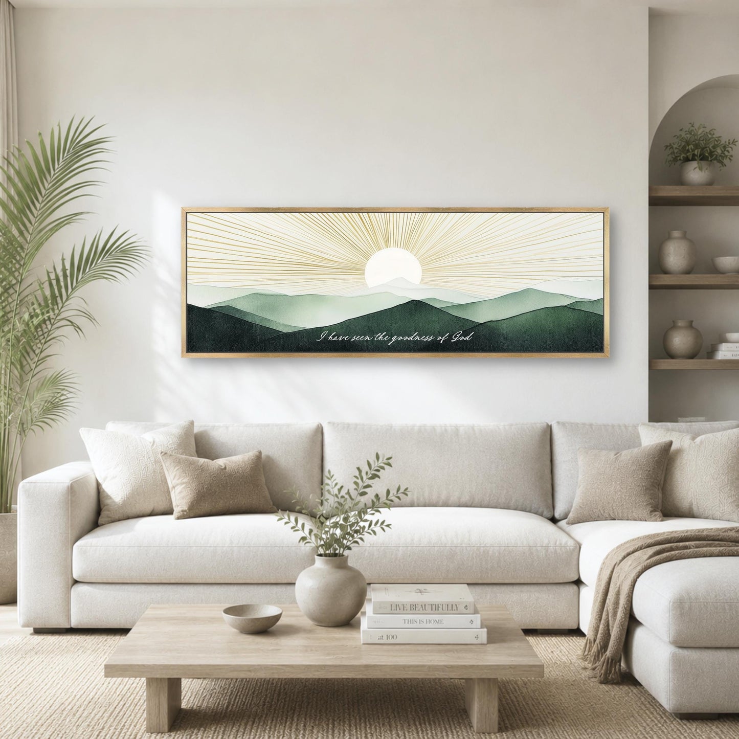 a living room with a large framed artwork depicting a serene landscape with mountains and a sun-like design in the sky. The artwork is mounted on the wall above a white sofa, which is positioned in front of a wooden coffee table. The room also includes a potted plant, a vase with greenery, and a bookshelf with various decorative items.