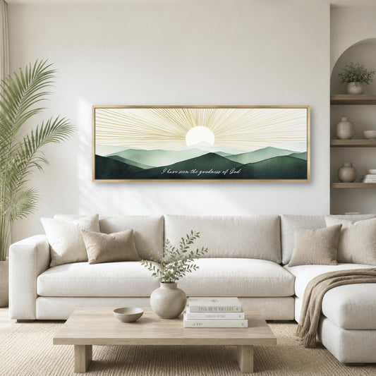 a living room with a large framed artwork depicting a serene landscape with mountains and a sun-like design in the sky. The artwork is mounted on the wall above a white sofa, which is positioned in front of a wooden coffee table. The room also includes a potted plant, a vase with greenery, and a bookshelf with various decorative items.
