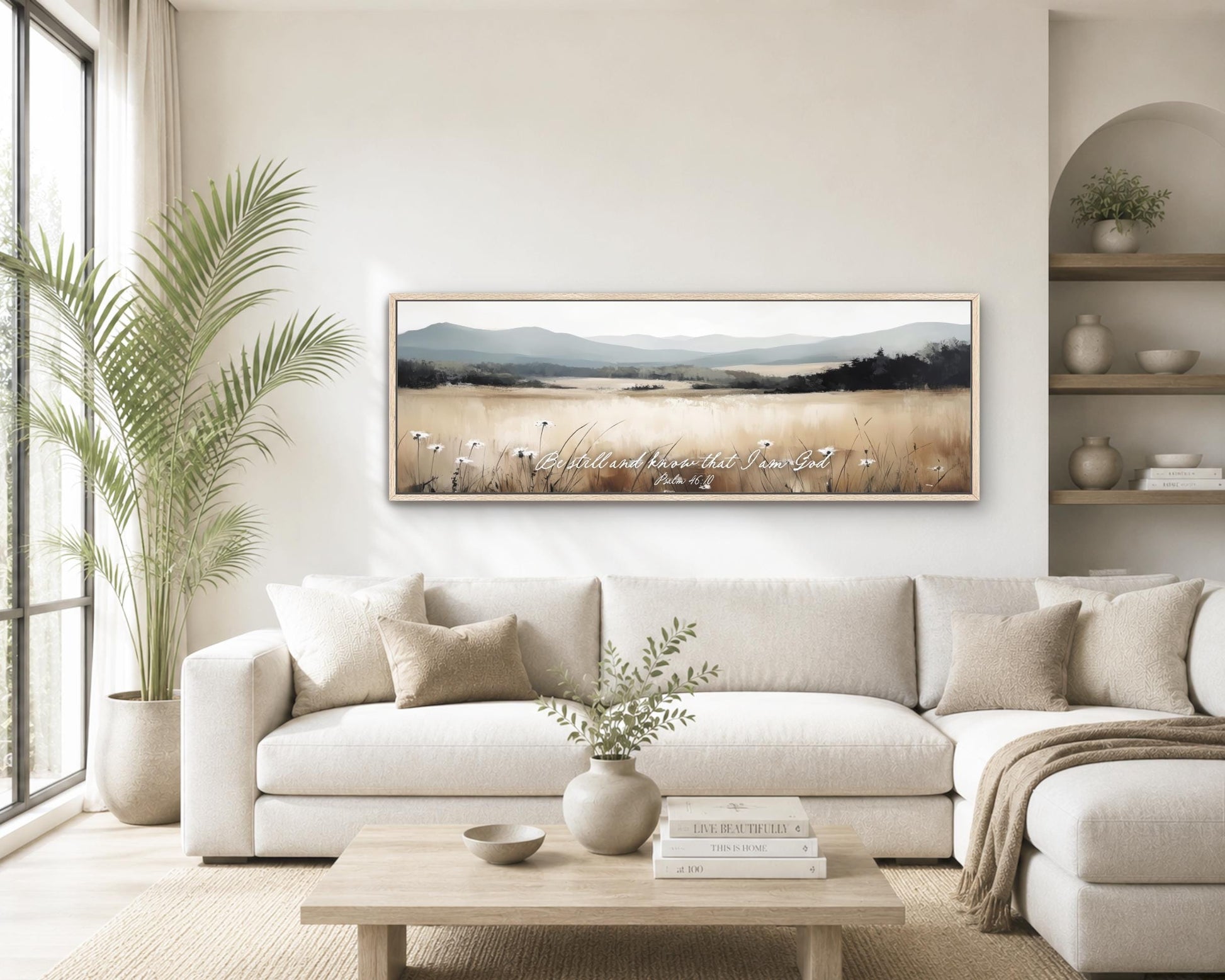 a serene living room with a large, framed landscape painting hanging on the wall above a white sofa. The painting features a field of flowers and mountains in the background, creating a peaceful and natural atmosphere. The room is decorated with various plants, vases, and books, contributing to a cozy and inviting ambiance.