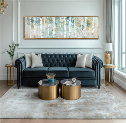A modern living room with a blue tufted sofa, two round coffee tables, and a large painting on the wall.