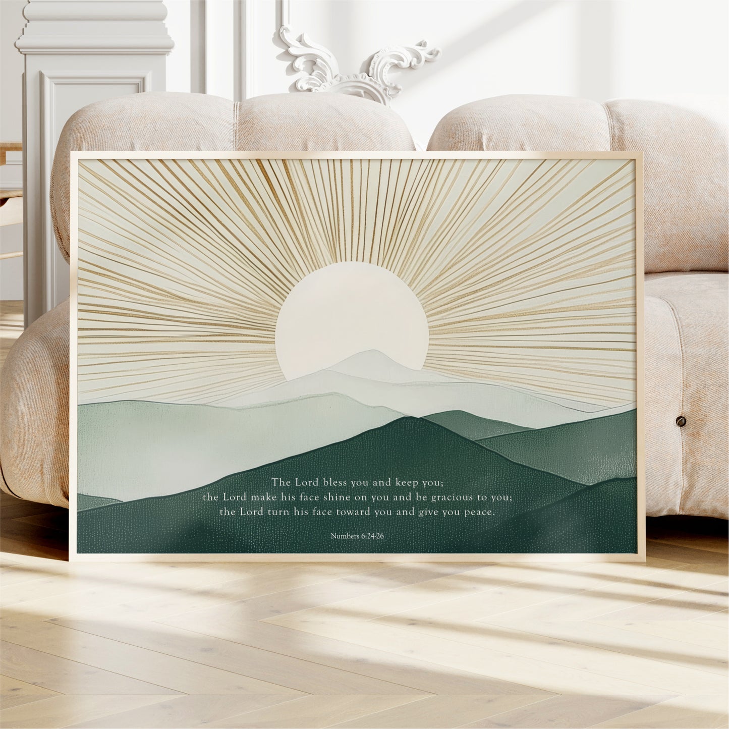 a framed poster with a serene landscape depicting a sun rising over a mountain range. The poster is placed on a wooden floor, with a white couch visible in the background.