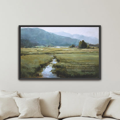 The image is a framed painting of a serene landscape with a winding stream, surrounded by mountains and lush greenery. The painting is hung on a wall above a beige couch, creating a peaceful and inviting atmosphere in the room.
