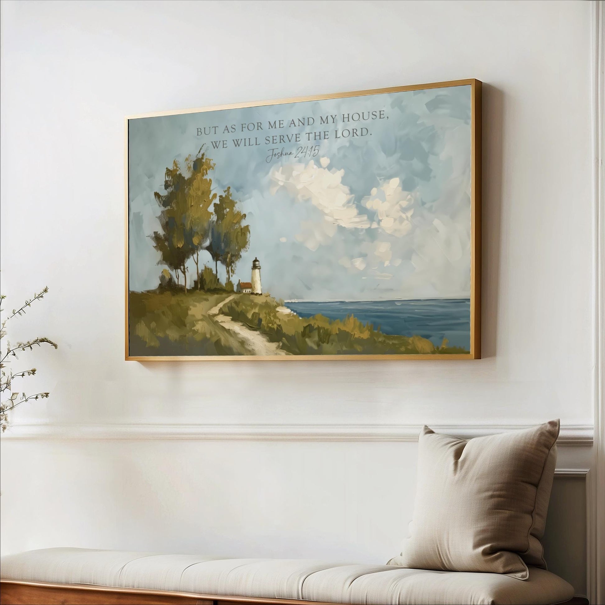 A framed painting of a lighthouse on a cliff overlooking the ocean hangs on a white wall, accompanied by a pillow and a plant in the foreground.