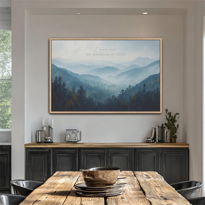 a large framed picture of a mountain landscape hanging on a wall above a wooden dining table with a bowl on it.