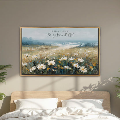 a framed painting of a field of white flowers hanging on a wall above a bed with white pillows.
