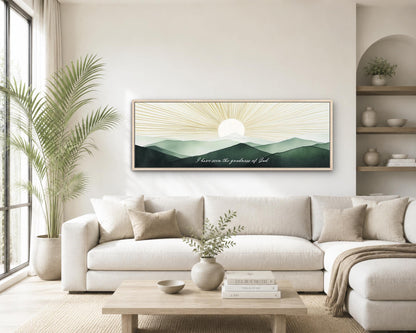 A living room with a large white sofa, a wooden coffee table, and a framed landscape painting depicting a sunrise over mountains.